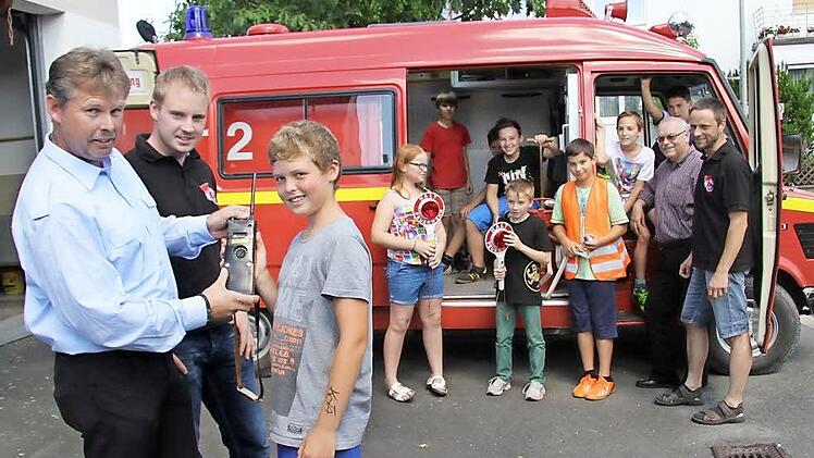Kommandant Christopher Stübinger und der Vorsitzende Torsten Grampp erklären Lukas Leitner (12), wie man ein Funkgerät richtig benutzt. Im Hintergrund erkunden die anderen Feuerwehrkinder das Auto: Larissa Grampp (11), Leon Wienoreck (10), Moritz Schatz (9), Johannes Michel(12), Jonas Ostbonk (8), Fabio Täuber (11), Jasper Hain (9) sowie Jakob Michel (10) mit Stadtrat Lothar Seyfferth und dem stellvertretenden Kommandanten Heiko Hofmann, der die neue Kindergruppe leitet.  Foto: Sonja Adam