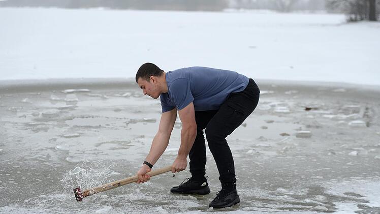 Mit einer Axt schl&auml;gt Merlin Hummel ein Loch ins Eis.