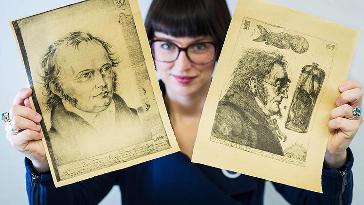 Julia Knapp, Geschäftsführerin des Vereins Jean Paul 2013, hat zwei Drucke des Künstlers Stephan Klenner-Otto in Händen, die Jean Paul (links) und dessen Romanfigur "Dr. Katzenberger" zeigen. Eine Ausstellung mit Illustrationen Klenner-Ottos unter dem Titel "Ein Radierer sieht Jean Paul" wird am 21. März in der Coburger Stadtbücherei eröffnet.  Foto: David Ebener/dpa