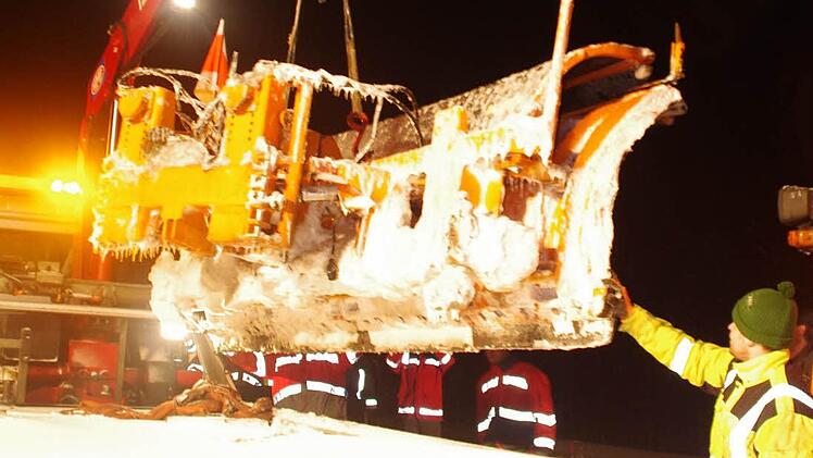 Der Kran eines Abschleppfahrzeuges befördert das schwere Räumschild des ausgebrannten Lastwagens auf die Ladefläche.