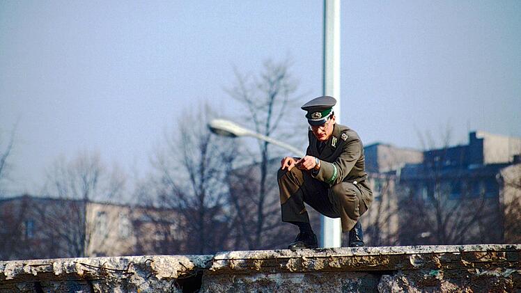 Ein DDR-Grenzer auf der Mauer ermahnt wahrscheinlich Personen auf der Straße.