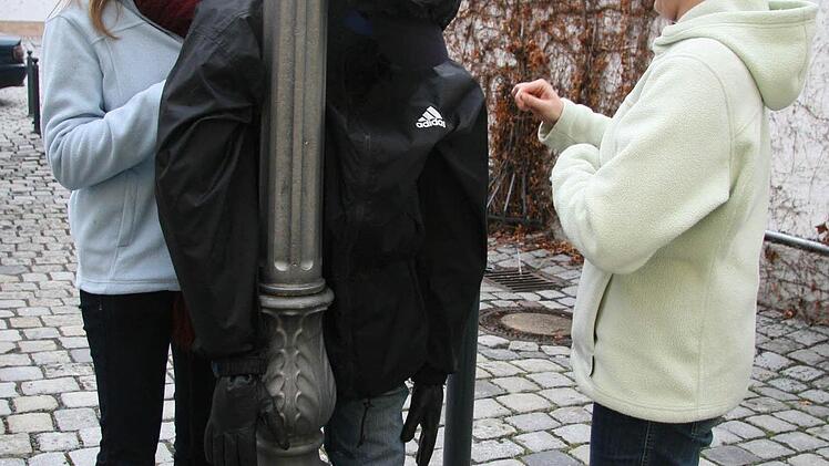 Juliana und Alena Wich befestigen den "Betrunkenen" mit der dunklen Adidas-Jacke an einem Laternenpfahl hinterm Rathaus.