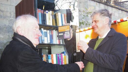 Hans-Jürgen Greve (rechts) bringt im Beisein von Lions-Freund Ulrich Strempel den QR-Code am offenen Bücherschrank an. Foto: Heike Scghülein
