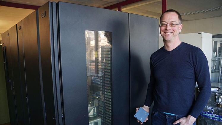 Marcel Ritter, stellvertretender Leiter des RRZE, zeigt vor dem alten Backup-System ein Magnetband, mit dem Daten von FAU-Fakult&auml;ten gesichert werden.    Foto: Pascale Ferry