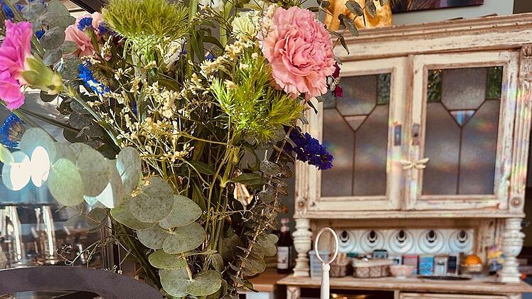 Einladendes Caf&eacute; mit Blumen, einem dreist&ouml;ckigen Tablett voller Geb&auml;ck, einem Kuchen und einem Schild mit italienischem Gru&szlig;. Ein gem&uuml;tlicher und einladender Ort f&uuml;r G&auml;ste.
