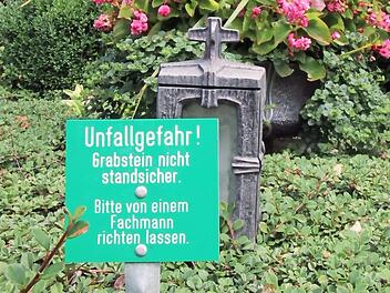 "Unfallgefahr! Grabstein nicht standsicher. Bitte von einem Fachmann richten lassen", steht auf den Hinweisschildern.
