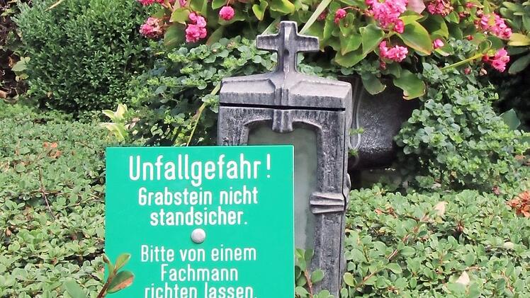 "Unfallgefahr! Grabstein nicht standsicher. Bitte von einem Fachmann richten lassen", steht auf den Hinweisschildern.