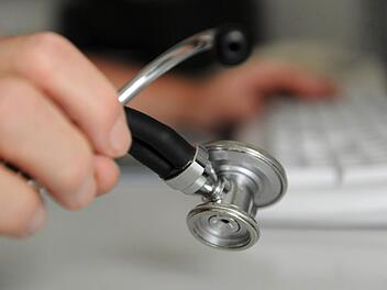 Ein Arzt hält ein Stethoskop in der Hand, mit der anderen Hand bedient er eine Computertastatur. Die Bürokratie nimmt zu, finden viele Mediziner. Foto (Archiv): Marijan Murat/dpa