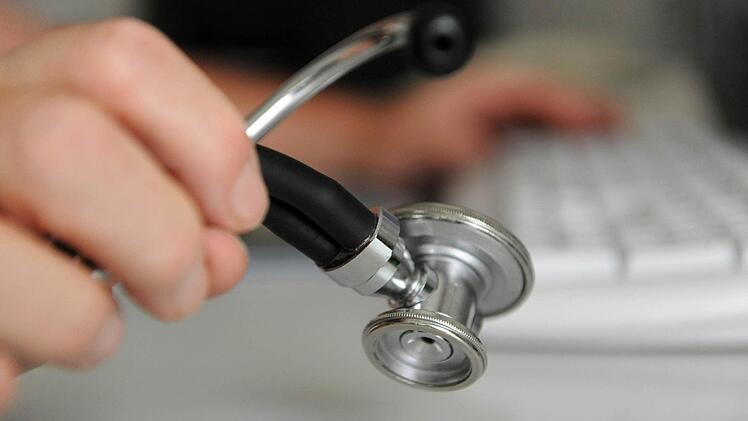 Ein Arzt hält ein Stethoskop in der Hand, mit der anderen Hand bedient er eine Computertastatur. Die Bürokratie nimmt zu, finden viele Mediziner. Foto (Archiv): Marijan Murat/dpa