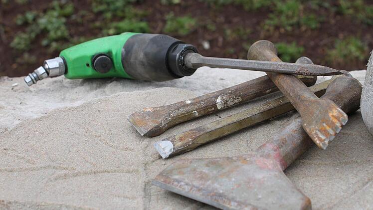Der grüne Hammer mit Pressluft liegt neben traditionellem Handwerksgerät.