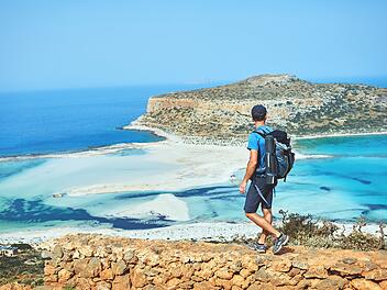 Rückenansicht eines Wanderers mit kleinem Rucksack auf dem Weg zum Strand von Balos am frühen Morgen. Balos Strand im Hintergrund, Kreta, Griechenland, back view of hiker with small backpack on the trail to the Balos beach at early morning. Balos beach on background, Crete, Greece, Balos ist eine Bucht mit einer hinter ihr befindlichen Lagune an der Westküste der griechischen Mittelmeerinsel Kreta. Sie befindet sich in der Gemeinde Kissamos des Regionalbezirks Chania.
