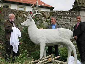 Wilfried Beck (ehemaliger Diakon am Volkersberg), Klaus Hofmann (Rektor Haus Volkersberg) und Marco Dietz (Sparkasse Bad Kissingen) freuen sich über die neue Skulptur des Sagentiers weißer Hirsch, die auf dem Volkersberg enthüllt wurde. Foto: Ralf Sauer