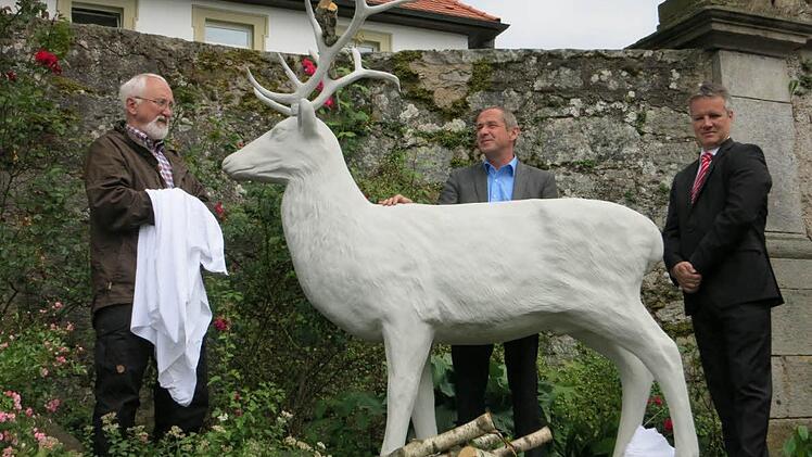 Wilfried Beck (ehemaliger Diakon am Volkersberg), Klaus Hofmann (Rektor Haus Volkersberg) und Marco Dietz (Sparkasse Bad Kissingen) freuen sich über die neue Skulptur des Sagentiers weißer Hirsch, die auf dem Volkersberg enthüllt wurde. Foto: Ralf Sauer