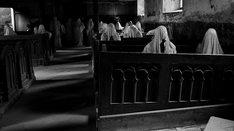 Lukov&aacute; St.-Georgs-Kirche Kirche Kirchenruine Geisterkirche Wei&szlig;e Figuren Verh&uuml;llte Gestalten Betende Figuren Holzb&auml;nke Kirchenb&auml;nke Stille Andacht Sakralraum Verfall Lost Place Dark Tourism Horror Reiseziele Europa Gruselige Orte Tschechien Westb&ouml;hmen Installation Kunst Mahnmal Ehemalige Bewohner Erinnerung Geschichte Atmosph&auml;re G&auml;nsehaut Unheimlich Fotomotiv Reise Inspiration Every day, dozens of white-clad figures sit quietly on its wooden benches with their heads bowed, humbly praying to God. The white figures, representing former residents of Lukova.