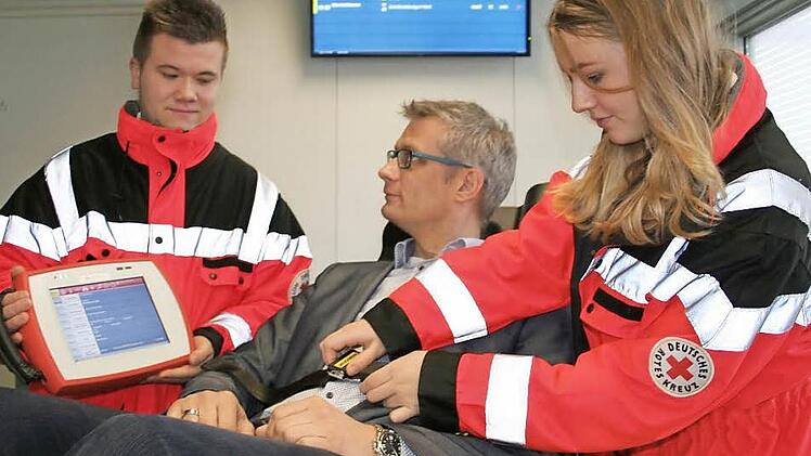 Oberbürgermeister Uwe Kirschstein wird in der Notaufnahme von der auszubildenden Rettungssanitäterin Christina Hohe auf der Trage fixiert. Keine Sorge: Er simuliert nur einen Patienten, dessen Daten der Notfallsanitäter , links Azubi Marcel Mönius mit dem NIDA-Pad in der Hand, jetzt aus dem Rettungswagen auf den an der Wand hängenden Ankunfts-Monitor im Klinikum übertragen kann.  Foto: Andreas Oswald