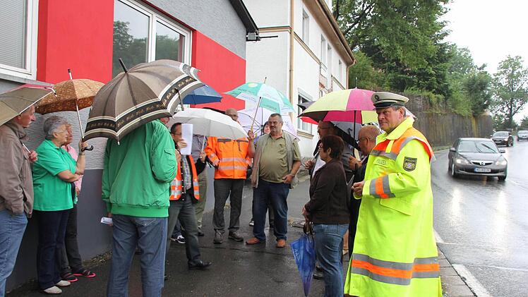 Die Anwohner aus Friedrichsburg besprachen am Donnerstag mit Behördenvertretern, wie der Unfallschwerpunkt entschärft werden kann. Derweil fuhren viele Autos und auch Laster an ihnen vorbei. Ursache für den Termin war der Lasterunfall vom 11. April, wo das Haus im Hintergrund stark beschädigt wurde.  Foto: Friedwald Schedel