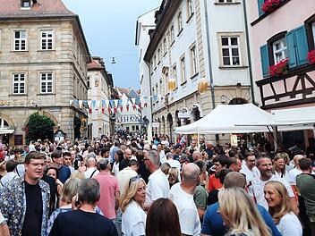 Menschenmassen füllen eine historische Straße bei der 75. Bamberger Sandkerwa, die mit bunten Wimpeln dekoriert ist. Fröhliche Gesichter genießen das Fest.
