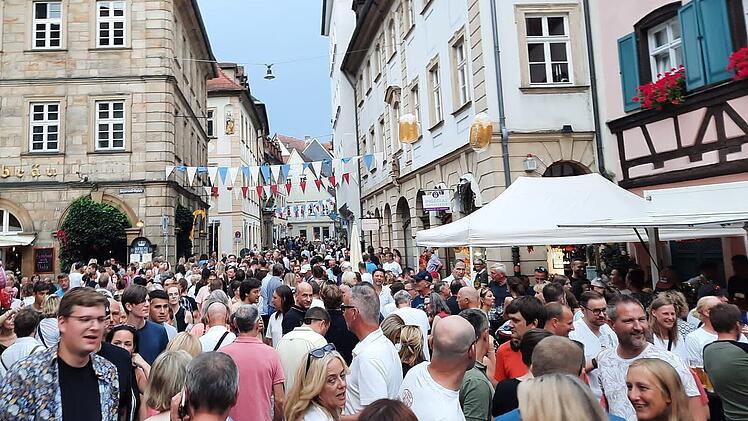 Menschenmassen füllen eine historische Straße bei der 75. Bamberger Sandkerwa, die mit bunten Wimpeln dekoriert ist. Fröhliche Gesichter genießen das Fest.