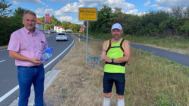 Michelau meets Michelau: Mit seinem Hobbylauf von Michelau in Oberfranken nach Michelau im Steigerwald hatte Bertram Wich (rechts) die sportliche Herausforderung angenommen, die knapp 80 Kilometer lange Strecke als Läufer zurückzulegen. Als Botschafter der Korbmachergemeinde tauschte er mit dem Bürgermeister Michael Wolf am Ortsschild von Michelau im Steigerwald Erinnerungsgeschenke aus. Foto: Klaus Gagel