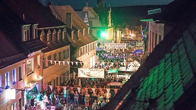 Ein gut besuchtes Stra&szlig;enfest in Sche&szlig;litz bei Nacht mit stimmungsvoller Beleuchtung, bunten Wimpeln und Live-Musik. Zahlreiche Menschen genie&szlig;en die festliche Atmosph&auml;re.