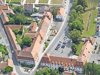 Familie Achtziger betreibt am Ebracher Marktplatz ein Café (hinter der Terrasse mit den roten Schirmen). Die vorgeschriebenen Parkplätze für die geplanten Gästezimmer auf dem dahinter liegenden Areal würde die Gemeinde in der Lagerhausstraße vermieten (links im Bild). Luftbild: Rinklef