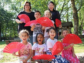 Joleen (vorne von links), Bethlehem, Amelia und Lilly sowie Paul (dahinter) und Lena vom Kindergarten St. Elisabeth wedeln sich mit den roten Fächern der Saale-Zeitung Luft zu. Leiterin Andrea Hippler (hinten links) und Mutter Yan Zao haben sich auch einen gesichert. Foto: Benedikt Borst