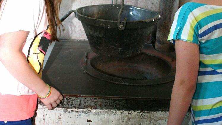 Lea und Luisa, zwei Ministrantinnen der Pfarrei Sankt Antonius, bestaunen den alten Holzofen. Wie in alten Zeiten wird im Kessel aus Zinn und Blei die Legierung für die Orgelpfeifen geschmolzen.