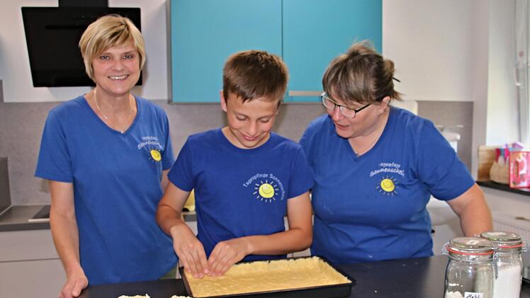 Fachkraft Marianne Krug (links) und ihre Kollegin Barbara Graumann geben Simon Tipps wie man ein Backblech mit Kuchenteig belegt.Helmut Will