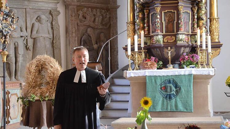 Pfarrer Gerald Munzert machte in seiner Ansprache das Erntedankfest schmackhaft, indem er regionale Produkte, wie hier einen geräucherten Schinken vom reichhaltigen Erntegabentisch in der St. Laurentius-Kirche vorstellte. Foto: Karl-Heinz Hofmann