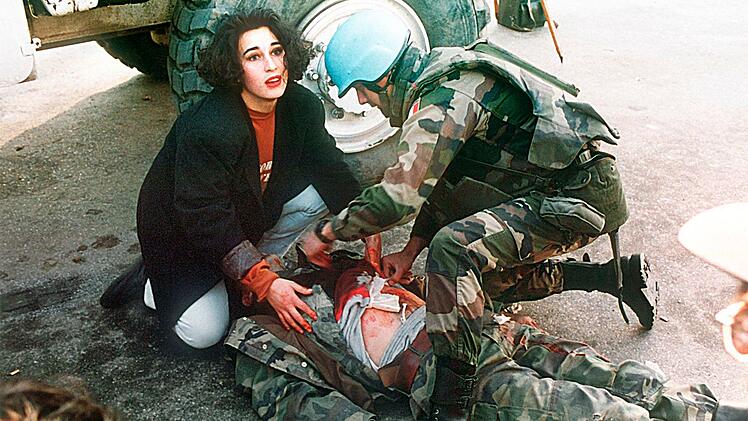 Die Fotografin f&auml;ngt den Moment ein, an dem w&auml;hrend des Bosnienkriegs eine Passantin bei Erste-Hilfe-Bem&uuml;hungen mitwirkt.