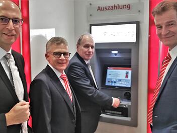 VR-Bank-Vorstand Roland Knoll (Mitte) versorgt sich im Beisein seines Vorstandskollegen Rainer Geis (links) sowie den Sparkassenvorständen Roland Friedrich (zweiter von links) und Michael Rendl (rechts) mit seiner VR-Bankkarte am Geldautomaten der Sparkasse mit Bargeld. Foto: Sigismund von Dobschütz