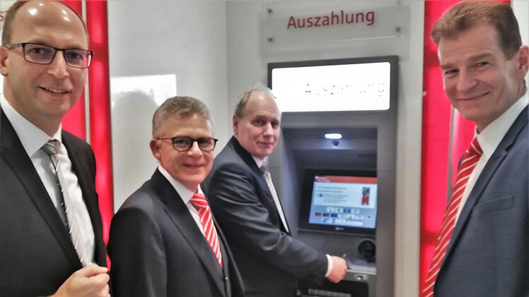 VR-Bank-Vorstand Roland Knoll (Mitte) versorgt sich im Beisein seines Vorstandskollegen Rainer Geis (links) sowie den Sparkassenvorständen Roland Friedrich (zweiter von links) und Michael Rendl (rechts) mit seiner VR-Bankkarte am Geldautomaten der Sparkasse mit Bargeld. Foto: Sigismund von Dobschütz