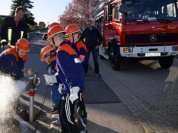 Linus hat es geschafft, das Ventil am Standrohr zu öffnen. Seine Mitstreiter von der Kinderfeuerwehr Wollbach schauen dabei zu. Kommandant Thomas Geis (links) schaut, ob sie es richtigmachen, ebenso Erwin Below (rechts). Foto: Kathrin Kupka-Hahn