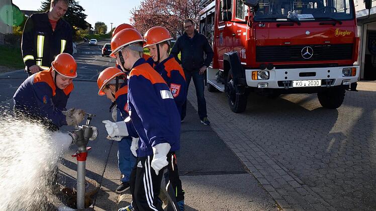 Linus hat es geschafft, das Ventil am Standrohr zu öffnen. Seine Mitstreiter von der Kinderfeuerwehr Wollbach schauen dabei zu. Kommandant Thomas Geis (links) schaut, ob sie es richtigmachen, ebenso Erwin Below (rechts). Foto: Kathrin Kupka-Hahn